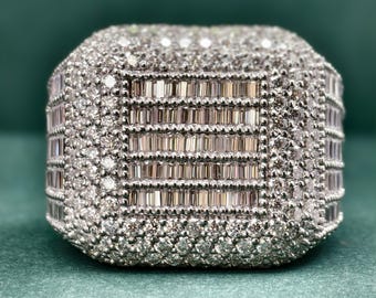 May include: A square-shaped ring with a large, intricate design of baguette and round diamonds set in white metal.