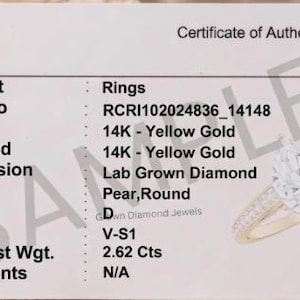 Puede incluir: Una tarjeta blanca de certificado de autenticidad con texto negro que detalla un anillo de oro amarillo de 14K con un diamante de laboratorio en forma de pera. La tarjeta enumera especificaciones como el número de estilo RCRI102024836_14148, color D, claridad V-S1 y un peso total de 2,62 quilates.