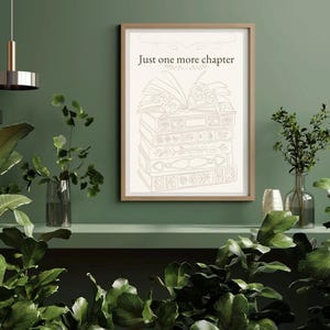 Peut inclure: Une affiche encadrée avec le texte "Just one more chapter" au-dessus d'une pile de livres. L'œuvre est de couleur beige clair, sur un mur vert. La pièce est décorée de plantes et de luminaires modernes.