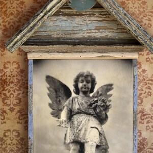 May include: A vintage photograph of an angel statue with wings, framed in a weathered wooden frame with a distressed blue paint finish. The frame is shaped like a house with a peaked roof.