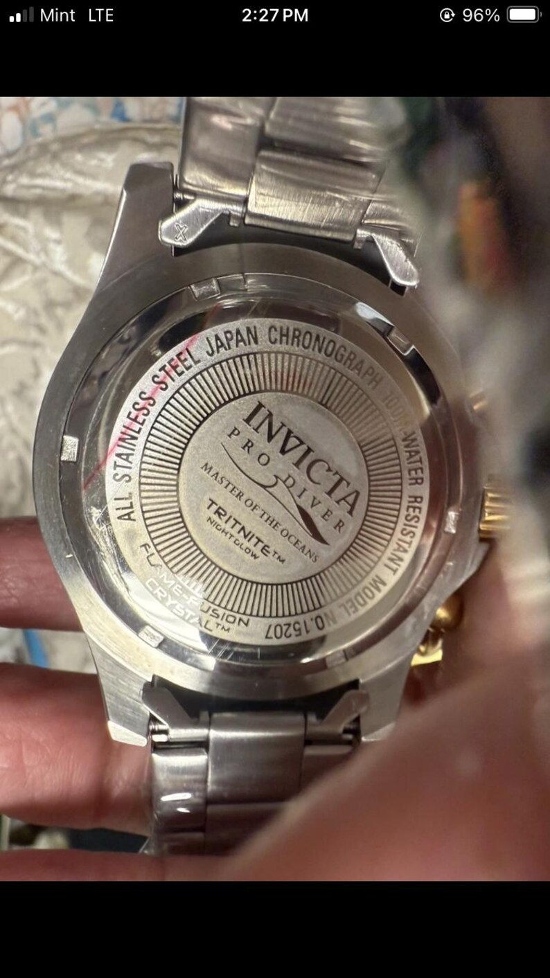 May include: Close-up of a stainless steel Invicta Pro Diver watch. The watch features a silver band and a round face with the text "All Stainless Steel Japan Chronograph 100M Water Resistant". The watch also has the text "Master of the Oceans" and "Tritnite Nightglow".
