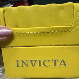 May include: Bright yellow watch box with the brand name "INVICTA" printed in gray. The box has a stitched edge and a slightly textured surface.