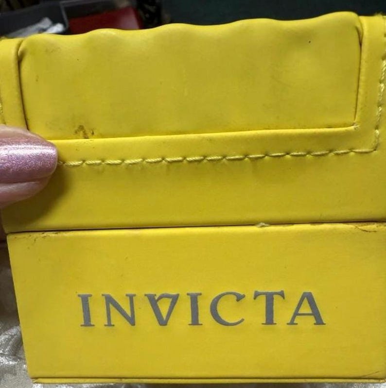 May include: Bright yellow watch box with the brand name "INVICTA" printed in gray. The box has a stitched edge and a slightly textured surface.