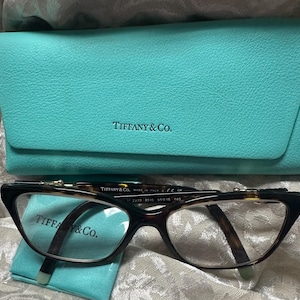 May include: A pair of tortoise shell eyeglasses with a Tiffany & Co. logo on the frame and a turquoise blue case with the Tiffany & Co. logo.