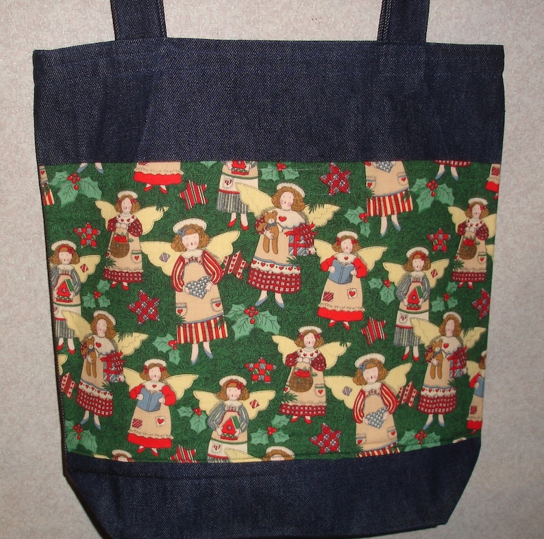 May include: A blue denim tote bag with a green fabric lining featuring a repeating pattern of angels with wings, holly, and stars. The angels are wearing red, white, and blue dresses and holding gifts.