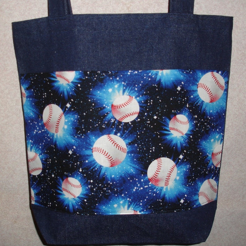 May include: A blue denim tote bag with a blue and white fabric lining featuring a repeating pattern of baseballs against a galaxy background.