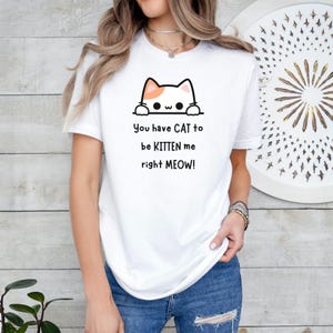May include: White t-shirt with a cat graphic and the text "You have CAT to be KITTEN me right MEOW!". The cat graphic is white with orange accents. The shirt is a casual style.