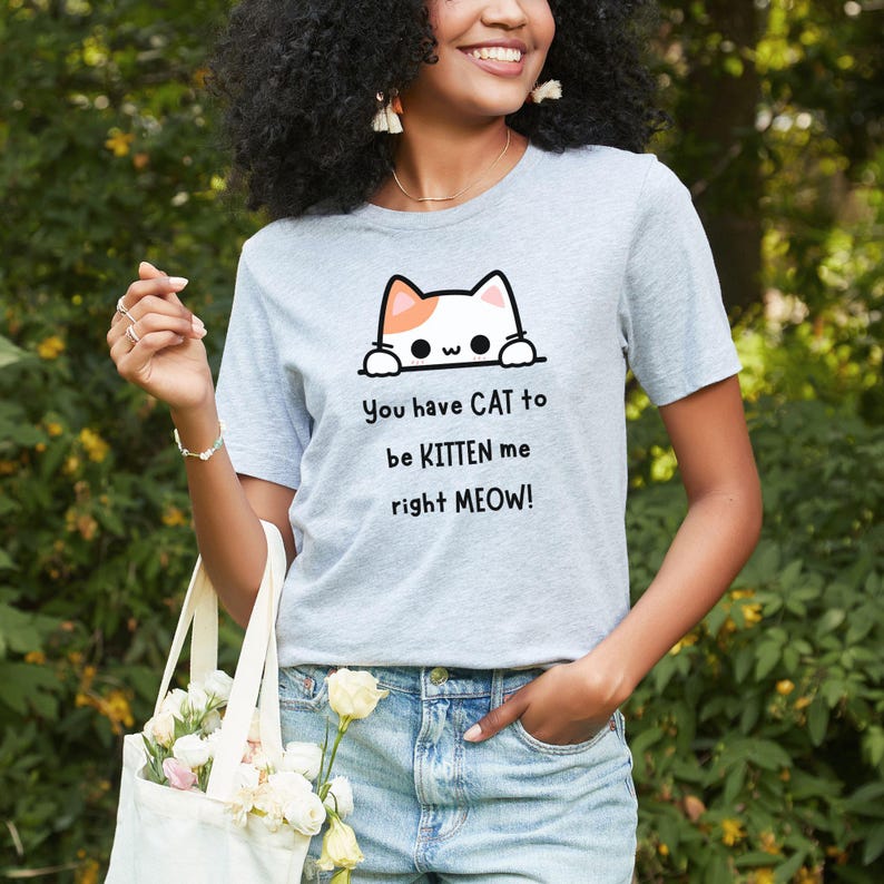 May include: Light gray t-shirt with a cat graphic and the text "You have CAT to be KITTEN me right MEOW!". The cat graphic is white with orange accents. The shirt is made of a soft material and has short sleeves.