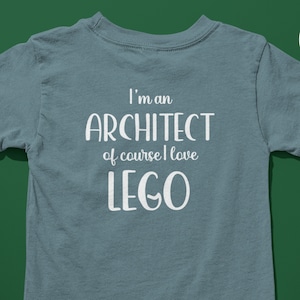 Puede incluir: Una camiseta azul claro con el texto "I'm an Architect of course I love LEGO" impreso en blanco en la parte posterior.