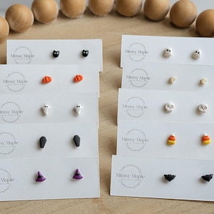 Pode incluir: Dez pares de pequenos brincos de pino exibidos em cartões brancos com o logótipo Mimsy Maple. Os designs incluem gatos pretos, abóboras cor de laranja, fantasmas brancos, caixões pretos, chapéus de bruxa roxos, caveiras brancas, doces de milho e morcegos pretos.
