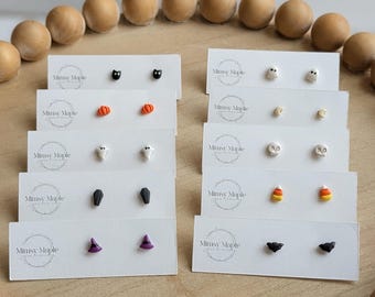 Könnte beinhalten: Zehn Paar kleine Ohrstecker auf weißen Karten mit der Aufschrift Mimsy Maple. Die Motive umfassen schwarze Katzen, orangefarbene Kürbisse, weiße Geister, graue Särge, violette Hexenhüte, weiße Geister, Monde, Totenköpfe, Zuckermais und schwarze Fledermäuse.
