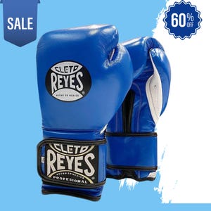 Op de afbeelding: Een paar blauwe bokshandschoenen met de merknaam "CLET0 REYES" in witte letters op een zwarte achtergrond. De handschoenen hebben een witte binnenkant en zwarte polsbanden. De afbeelding bevat ook een "SALE"-tag en een "60% OFF"-badge.