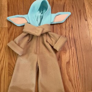 Peut inclure: Un ensemble de costume beige compos&eacute; d'une combinaison et d'une capuche assortie avec des d&eacute;tails bleus clairs et roses. Le costume est con&ccedil;u pour ressembler &agrave; un personnage d'une s&eacute;rie de science-fiction. L'ensemble est en tissu doux.