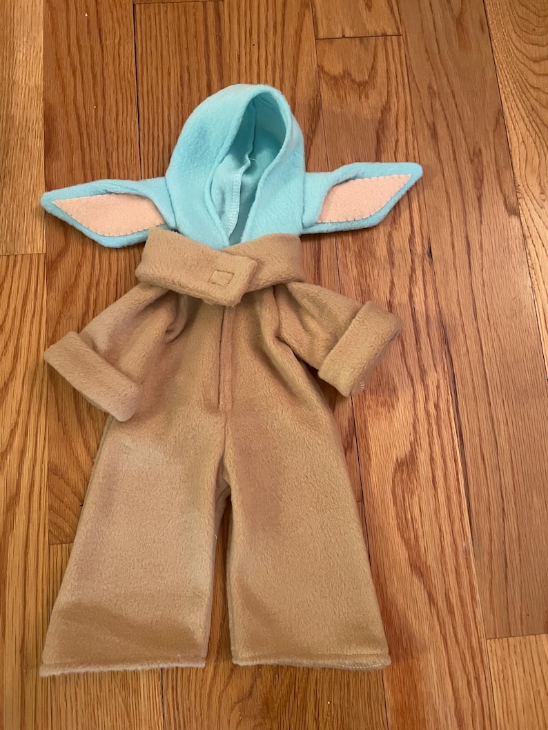 Peut inclure: Un ensemble de costume beige compos&eacute; d'une combinaison et d'une capuche assortie avec des d&eacute;tails bleus clairs et roses. Le costume est con&ccedil;u pour ressembler &agrave; un personnage d'une s&eacute;rie de science-fiction. L'ensemble est en tissu doux.