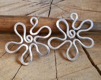 May include: A pair of silver metal earrings shaped like stylized flowers. The earrings are made of wire that has been twisted and shaped into a flower design.