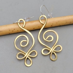 May include: A pair of gold-tone earrings with a swirling, abstract design. The earrings are made of wire and have a delicate, feminine look.