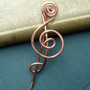 May include: A copper wire treble clef brooch, a musical symbol, with a long pin.