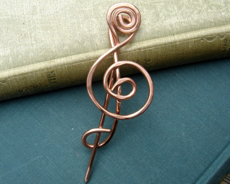 May include: A copper wire treble clef brooch, a musical symbol, with a long pin.