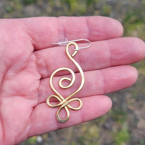 May include: Gold wire earring with a unique, abstract design. The earring is shaped like a stylized swirl with a loop at the top for hanging.