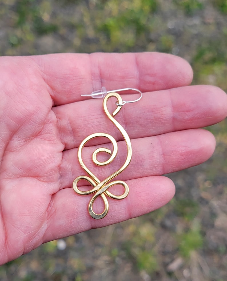 May include: Gold wire earring with a unique, abstract design. The earring is shaped like a stylized swirl with a loop at the top for hanging.