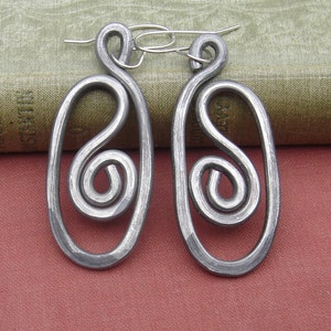 May include: A pair of silver metal earrings with a unique swirl design. The earrings are oval shaped and have a hammered finish.