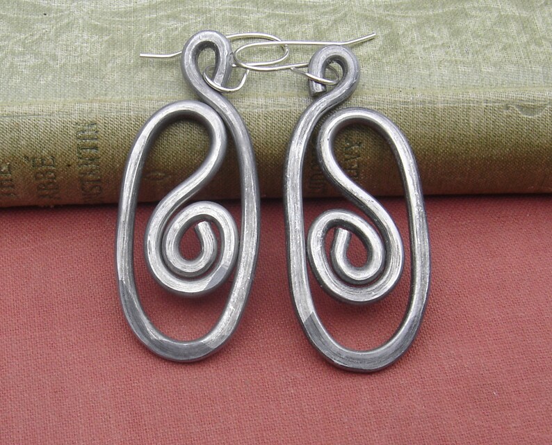 May include: A pair of silver metal earrings with a unique swirl design. The earrings are oval shaped and have a hammered finish.