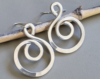 May include: A pair of silver earrings with a spiral design. The earrings are made of wire and have a simple, modern look.
