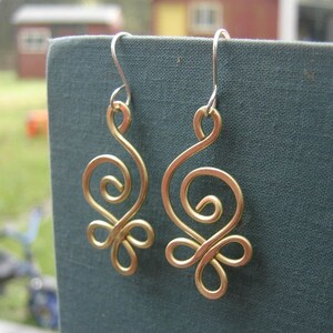 May include: A pair of gold-colored wire earrings with a swirling design. The earrings are hanging from silver hooks.