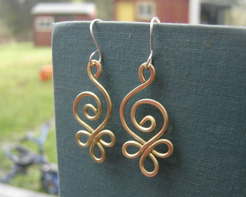 May include: A pair of gold-colored wire earrings with a swirling design. The earrings are hanging from silver hooks.