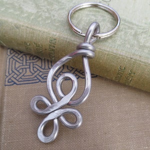 May include: Silver metal key chain with a decorative knot design. The knot is in the shape of a teardrop with a loop at the top.