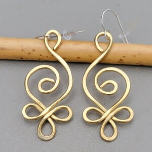 May include: A pair of gold-toned earrings with a unique, swirling design. The earrings are made of wire and have a delicate, feminine look.