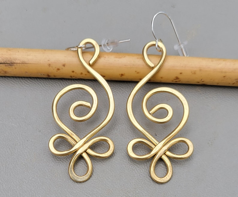 May include: A pair of gold-toned earrings with a unique, swirling design. The earrings are made of wire and have a delicate, feminine look.