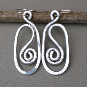 May include: A pair of silver earrings with a unique, abstract design. Each earring features a large oval shape with a smaller, twisted spiral inside.