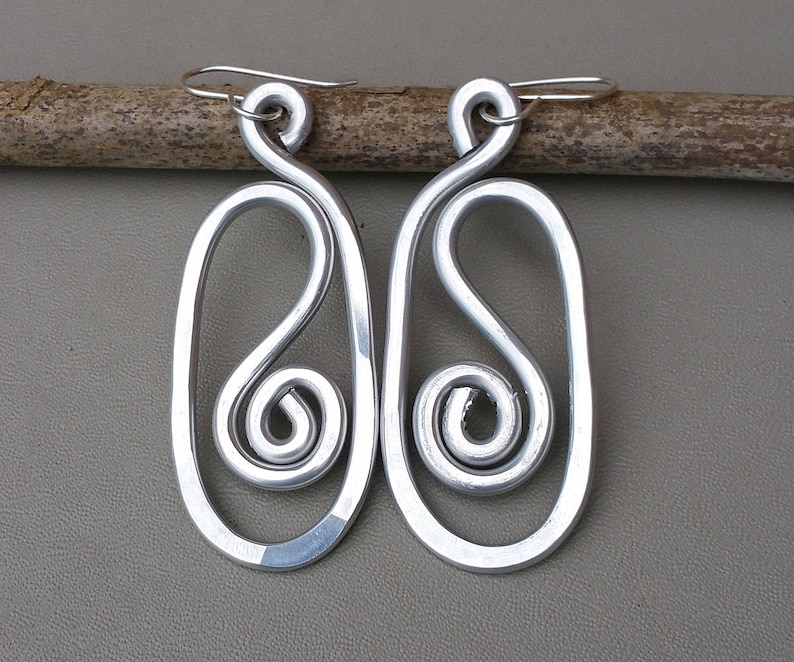 May include: A pair of silver earrings with a unique, abstract design. Each earring features a large oval shape with a smaller, twisted spiral inside.