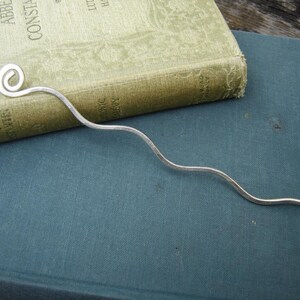May include: A silver bookmark with a curled end. The bookmark is laying on a blue book.