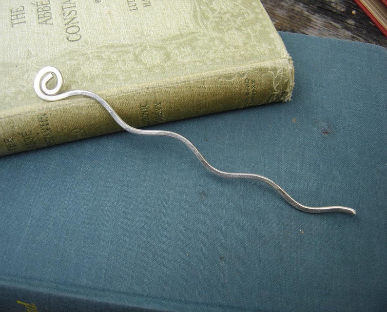 May include: A silver bookmark with a curled end. The bookmark is laying on a blue book.
