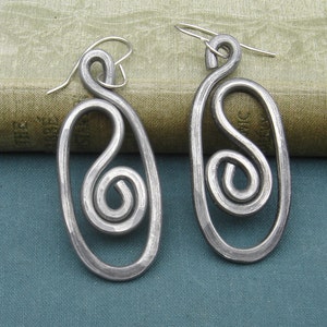 May include: A pair of silver earrings with a unique, abstract design. Each earring features a twisted, spiral shape within an oval frame.