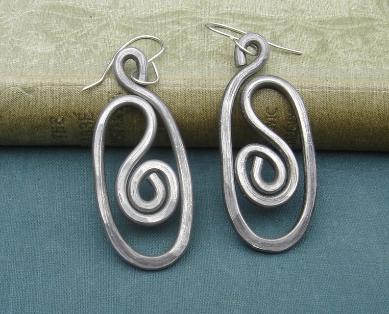 May include: A pair of silver earrings with a unique, abstract design. Each earring features a twisted, spiral shape within an oval frame.