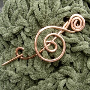 May include: A copper wire treble clef brooch pin on a green fuzzy fabric background.