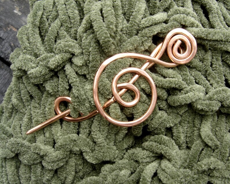 May include: A copper wire treble clef brooch pin on a green fuzzy fabric background.