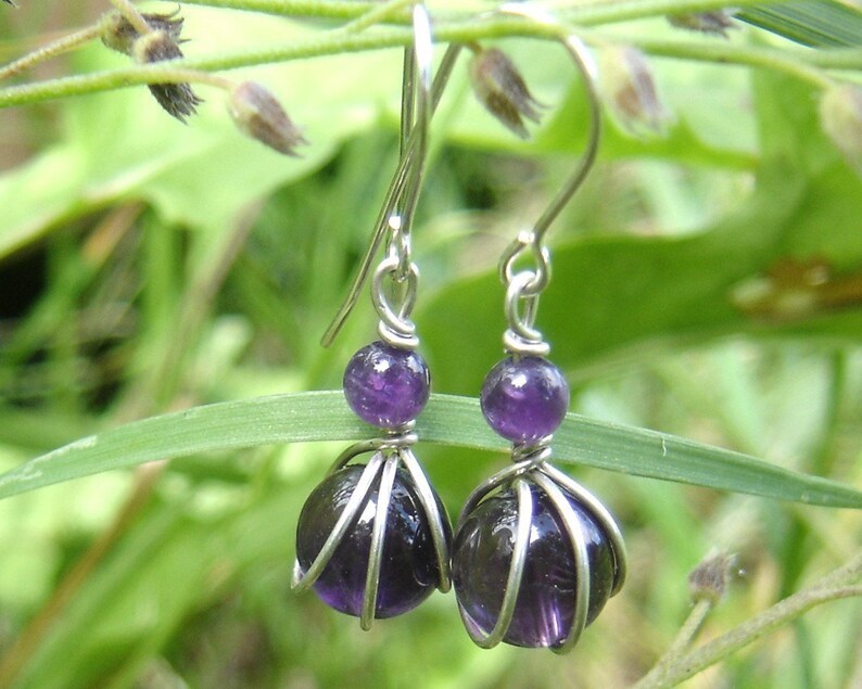 May include: A pair of silver earrings with amethyst gemstones. The earrings feature a wire cage design around each gemstone.