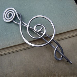 May include: Silver metal treble clef hair clip. The treble clef is a musical symbol.