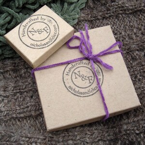 May include: Two brown cardboard boxes with a purple ribbon on one. Both boxes have a round stamp that says "Handcrafted by N&F nicholasandfelice.com".