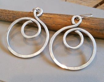 May include: A pair of silver earrings with a hammered finish. Each earring features a large circle with a smaller spiral inside.