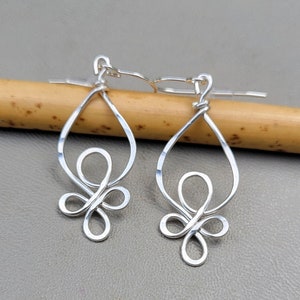 May include: A pair of silver dangle earrings with a twisted wire design and a knotted flower shape at the bottom.