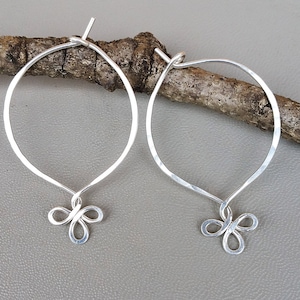 Könnte beinhalten: Ein Paar silberne Creolen mit einem Knotendesign. Die Creolen sind aus gehämmertem Silber gefertigt und haben einen zarten, femininen Look.
