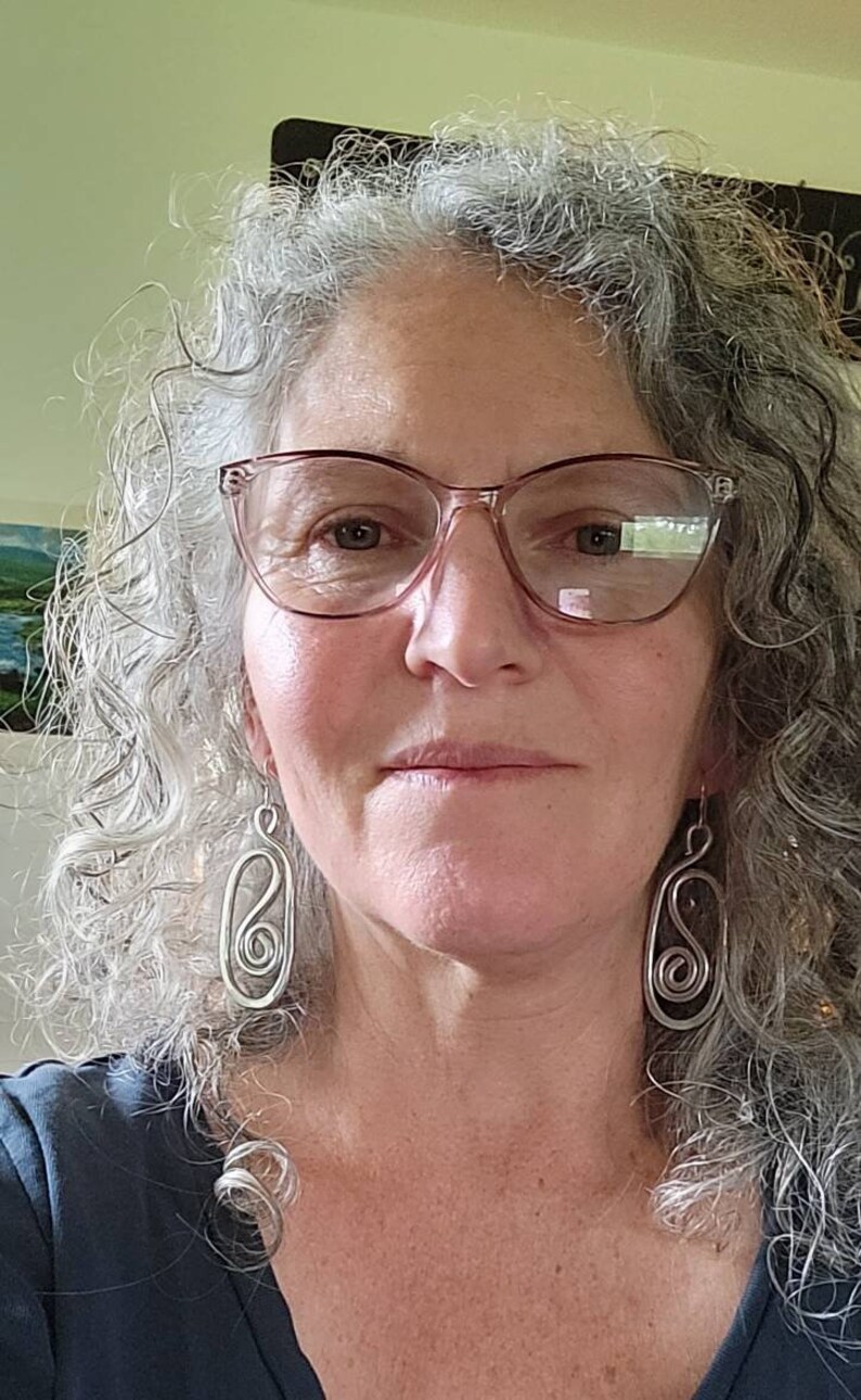 May include: A woman with gray curly hair wearing glasses and silver earrings. The earrings are shaped like a figure eight.