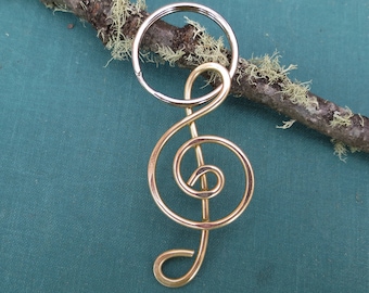 May include: A gold-colored treble clef keychain. The clef is made of wire and is attached to a silver-colored key ring.