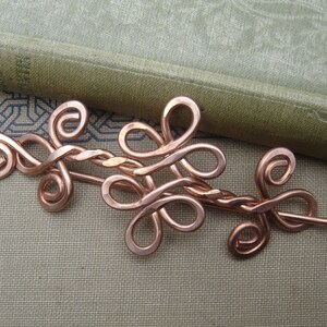 May include: A copper wire hair pin with a decorative design of intertwined loops and swirls.
