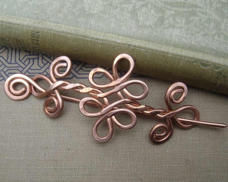 May include: A copper wire hair pin with a decorative design of intertwined loops and swirls.